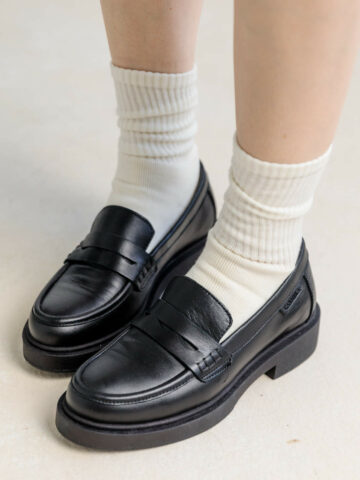 close up of woman wearing black leather loafers with white slouch socks.