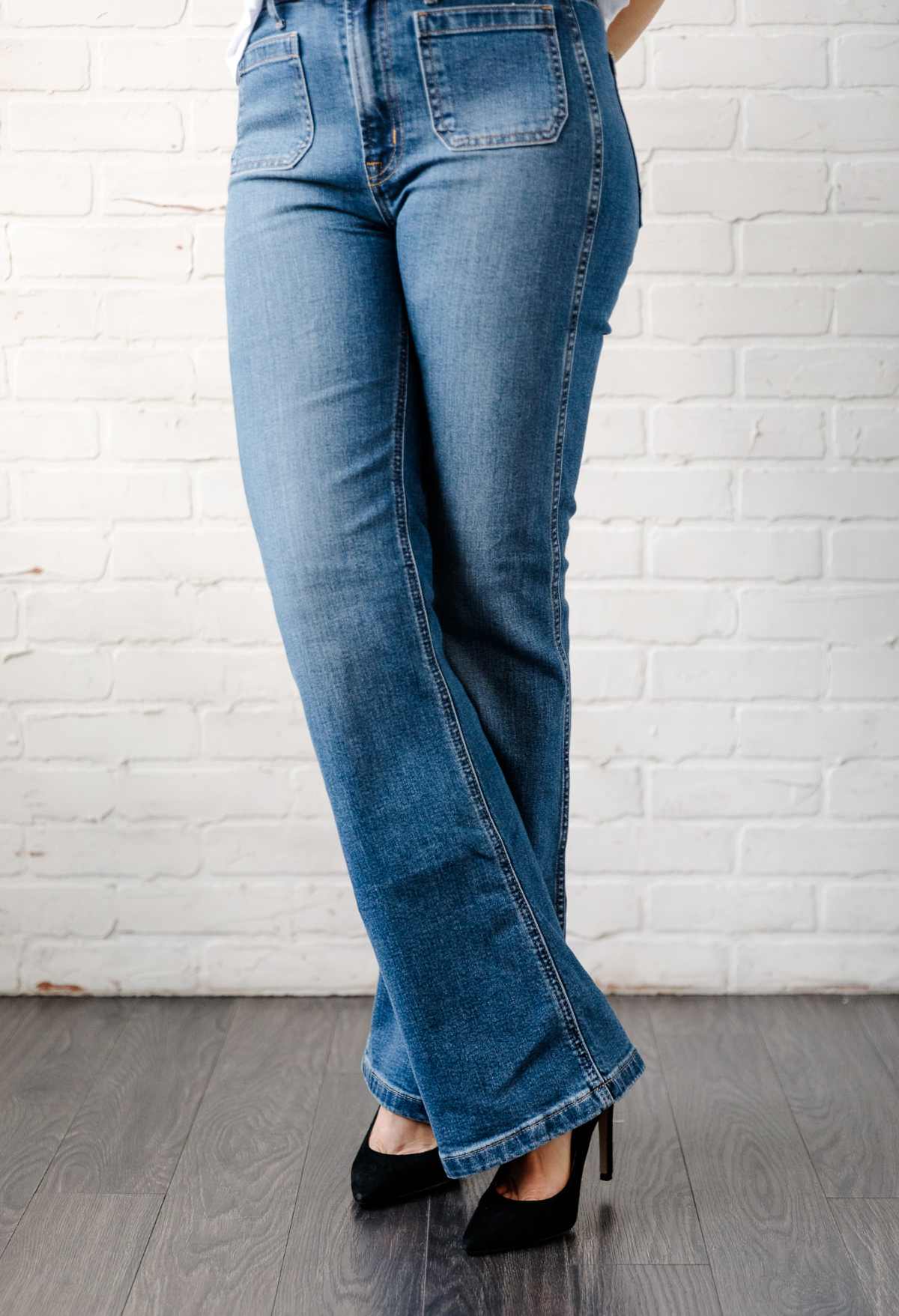 Close of up woman's legs wearing blue flared jeans with black stiletto heel pumps.