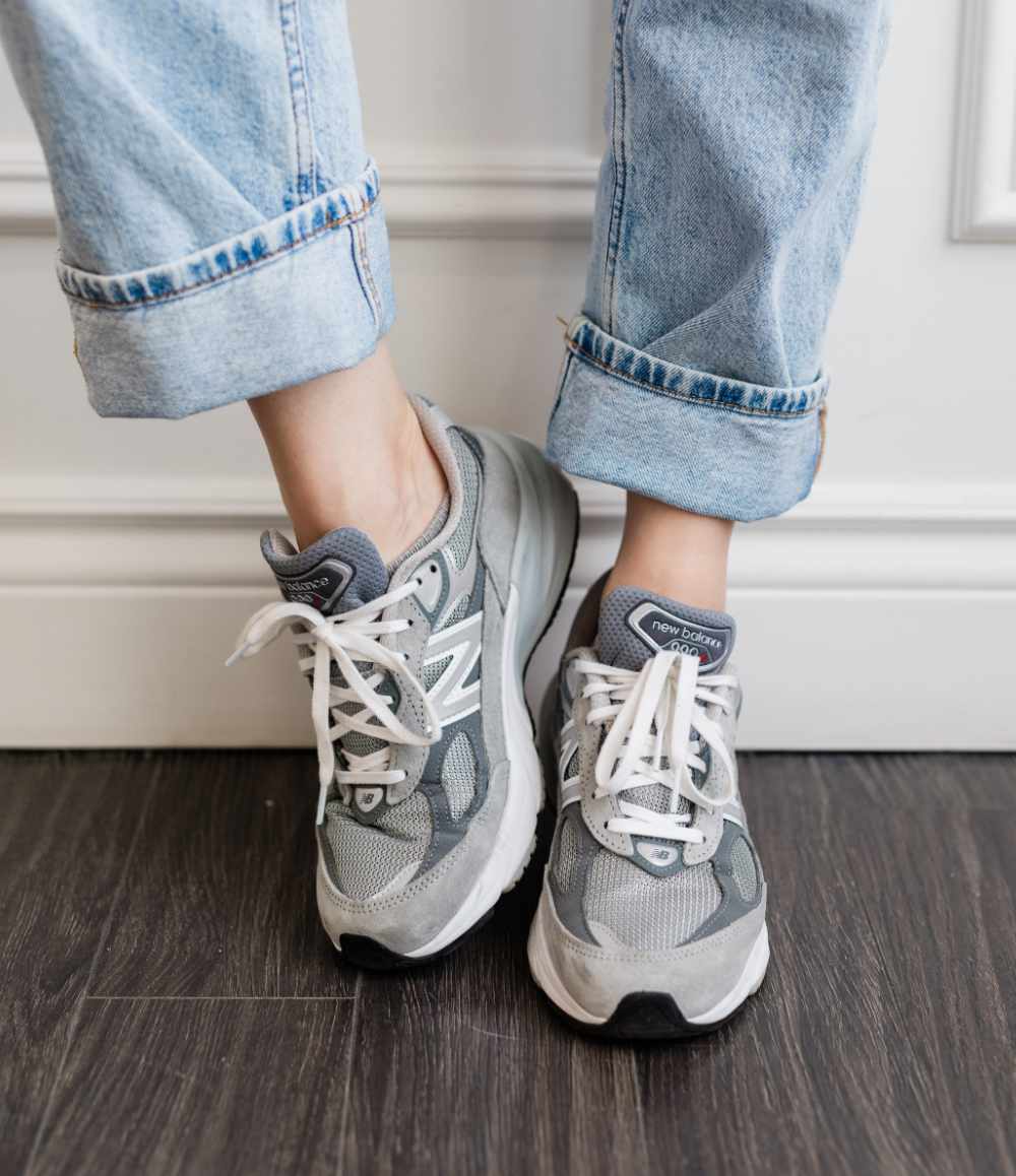 Close up of woman's legs wearing grey New Balance 990 V6 dad sneakers with rolled up faded straight leg jeans.
