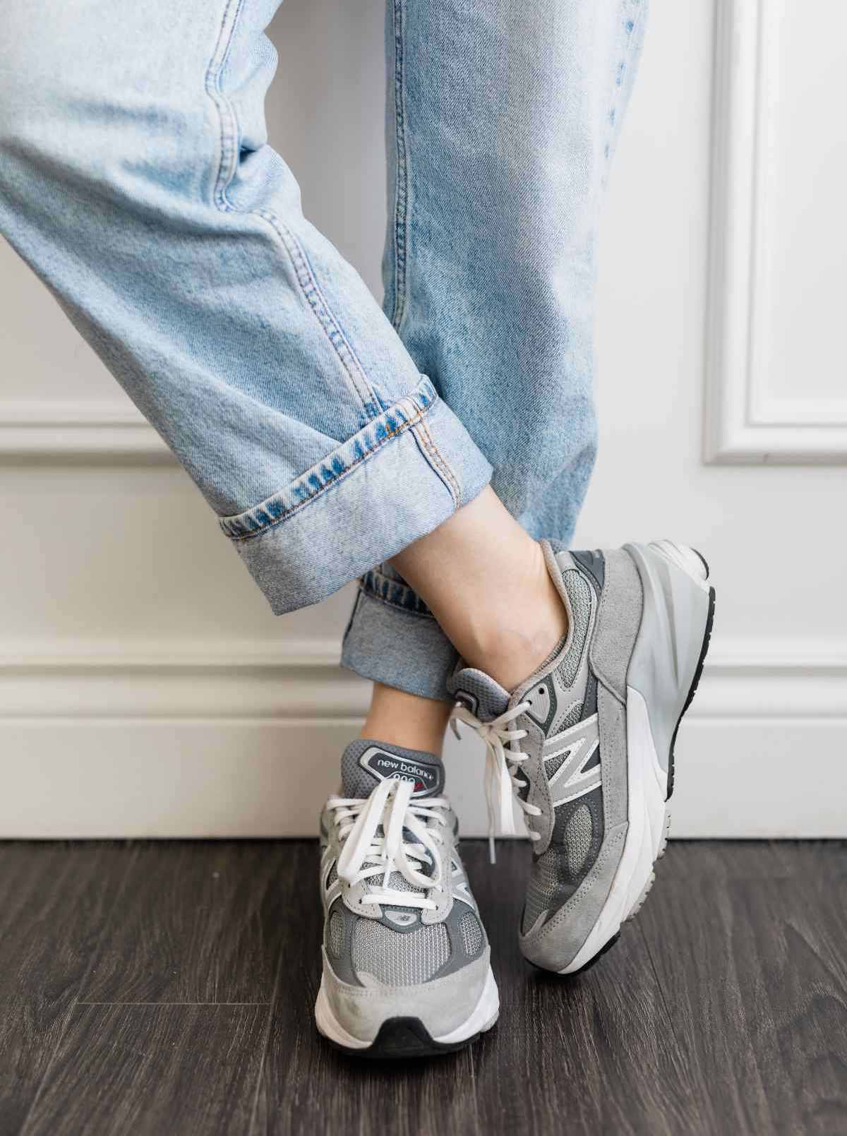 Close up of woman's legs wearing grey New Balance 990 V6 dad sneakers with rolled up faded straight leg jeans.
