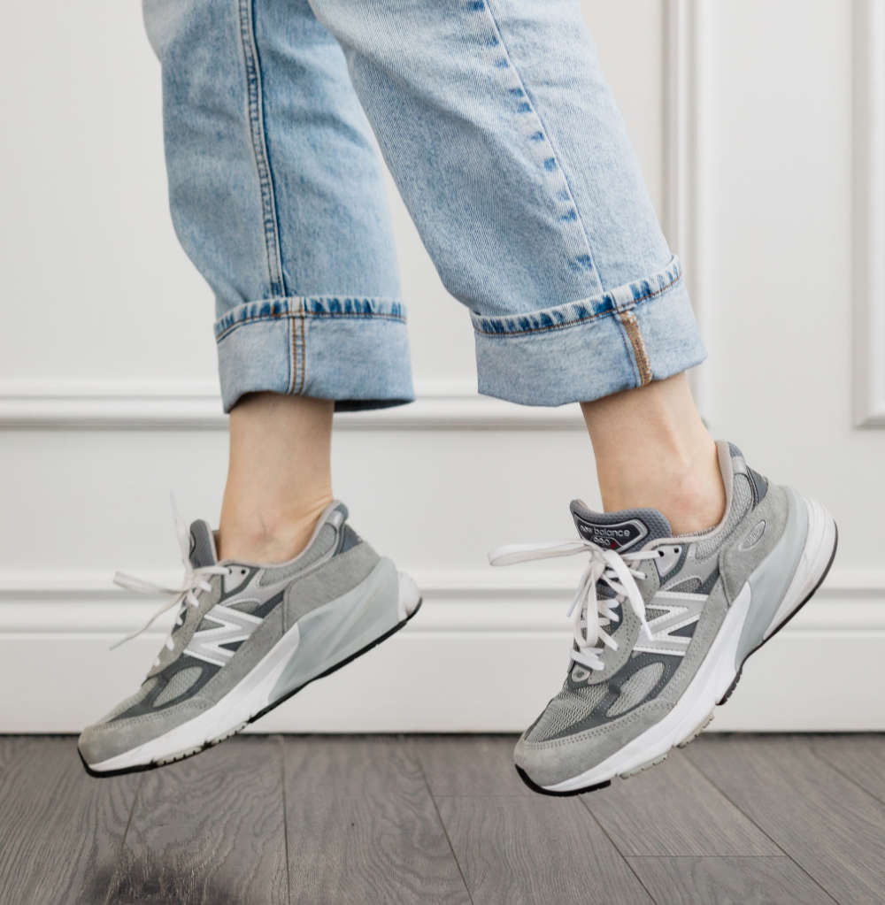 Close up of woman's legs jumping in grey New Balance 990 V6 dad sneakers with rolled up faded straight leg jeans.