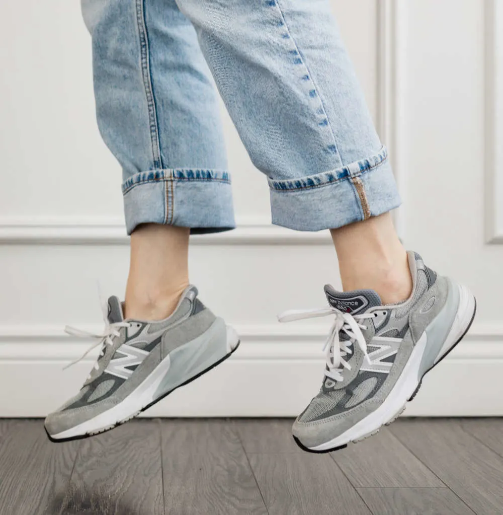 Close up of woman's legs jumping in grey New Balance 990 V6 dad sneakers with rolled up faded straight leg jeans.