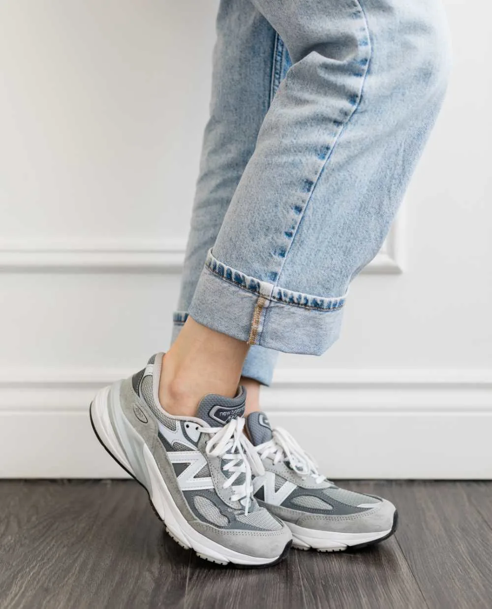 Close up of woman's legs wearing grey New Balance 990 V6 dad sneakers with rolled up faded straight leg jeans.