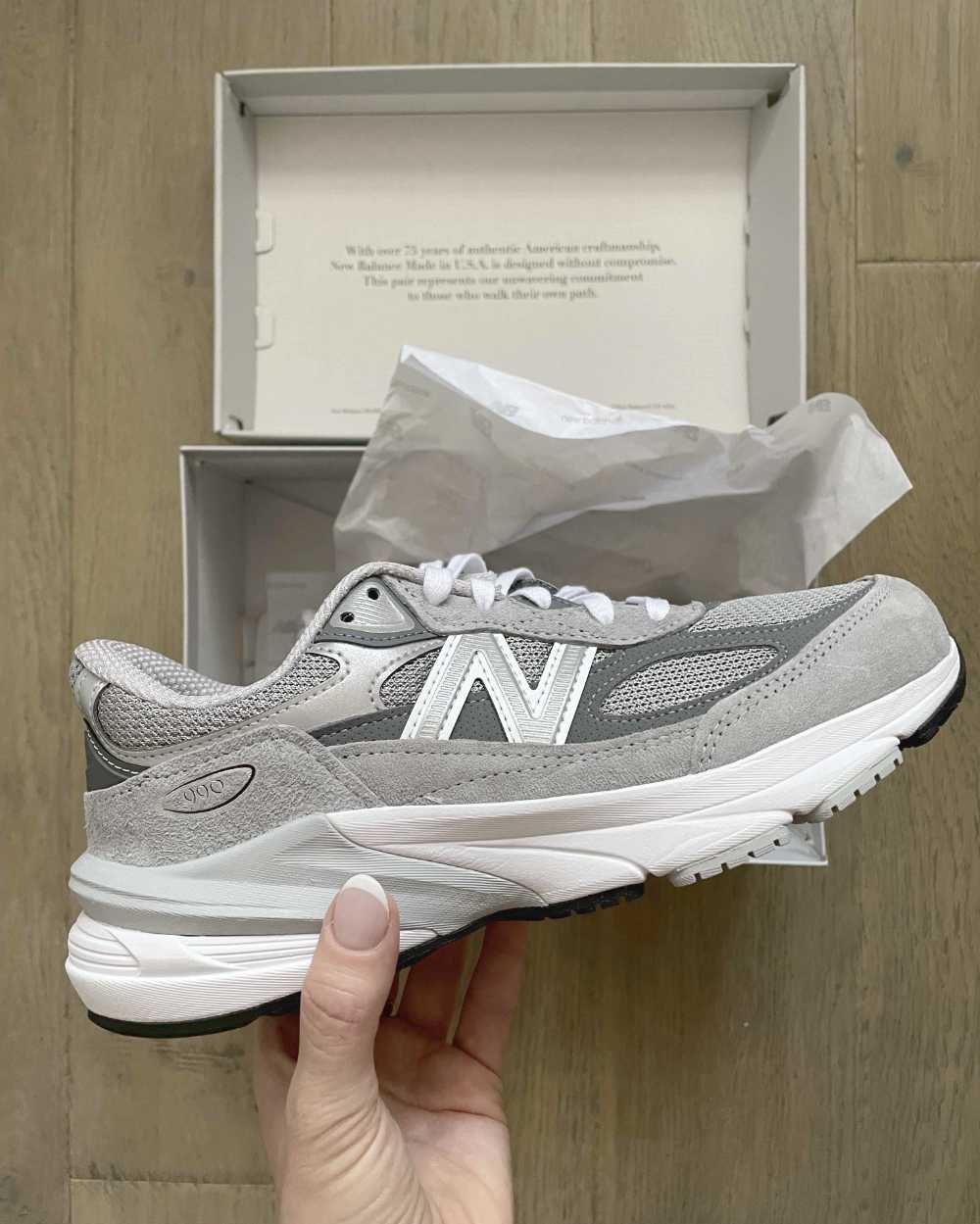 Close up of side view of grey and white New Balance 990 V6 with a hand unboxing the shoes. 