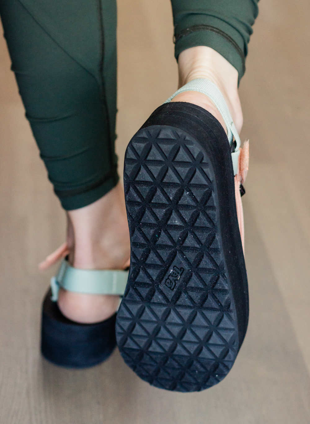 Close up outsole rear view of woman walking away wearing teva platform sandals with green leggings.