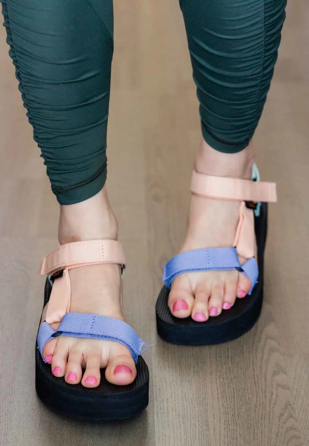 Close up front view of woman wearing teva platform sandals with green leggings.