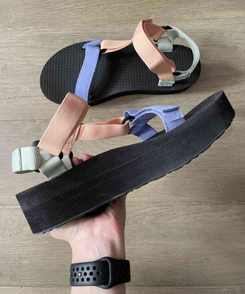 Top view of woman holding Teva platform sandals in hand on a wooden floor.