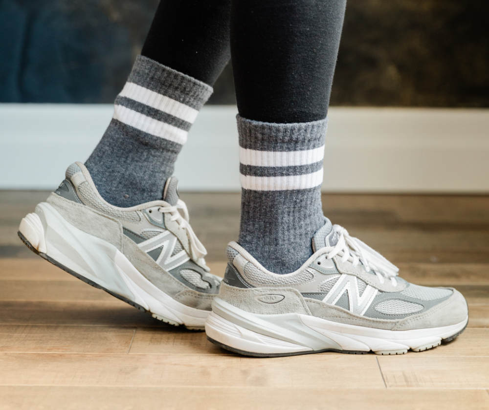 Close up of woman wearing grey in tone stripe crew socks with grey new balance 990 V6 dad sneakers. 